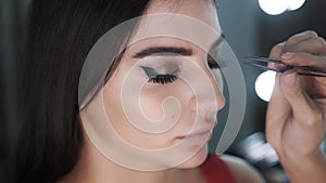 Close-up make-up artist sticks false eyelashes of a beautiful young female mode