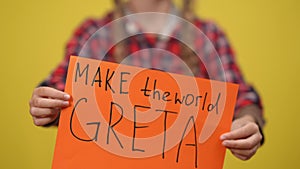 Close-up Make the world Greta call in female teenage hands at yellow background. Unrecognizable adolescent environmental