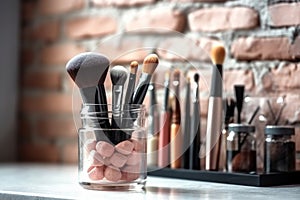 Close-up of makeup brushes in a glass jar on table in stylist room on light background, concept of women\'s cosmetics