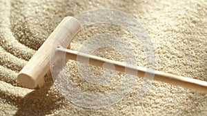 Close-up making sand zen garden using mini wooden rake with shadows and sunlight