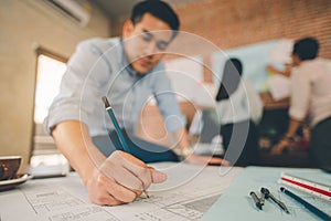 Close up of male architect hands writing model on the desk. Blurred behind team of engineer discussing of construction plan.