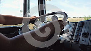 Close up male arms of lorry driver holds a big steering wheel while operating a truck at sunny day. Trucker riding to