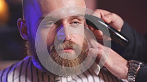 Close-up of male Barber trimming hair to client with electric razor.