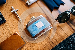Close-up of a male blue jar with brown leather inserts with a purse, sunglasses and a cross on a smooth wooden surface.