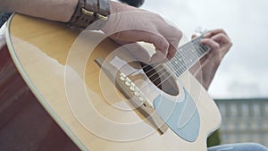 Close-up of male Caucasian fingers on guitar strings. Unrecognizable street musician playing musical instrument outdoors