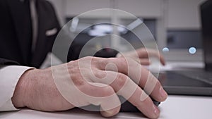 Close-up male Caucasian hand using computer mouse in office in slow motion. Unrecognizable man in formal suit surfing