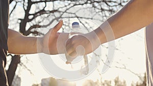 Close-up of male Caucasian hands sharing water on sunset in the autumn park. Two adult boys shaking hands in sunlight