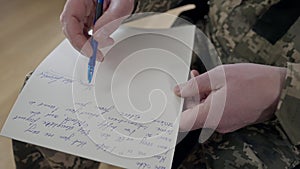 Close-up of male Caucasian middle aged hand writing letter with pen on paper. Unrecognizable military man sitting