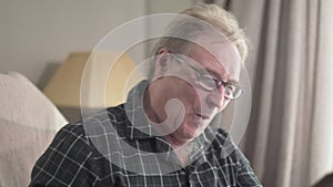 Close-up of male caucasian retiree laughing as watching photo album. Cheerful old man in eyeglasses enjoying recalling