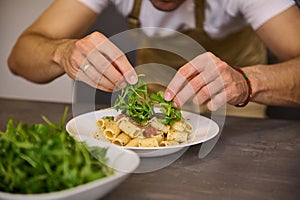 Close-up male chef hands garnishing Italian pasta with fresh green arugula leaves. Man cooking pasta according to