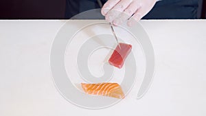 Close-up of male chef hands in gloves preparing delicious appetizer of fresh fish on a white table.