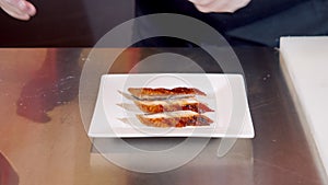 Close-up of male chef hands in gloves preparing delicious appetizer with pieces of smoked tuna on a plate