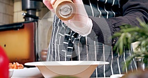 Close-up of male chef hands in gloves sprinkling spices and salt on a dish in a white plate. Cooking food in the restaurant