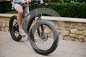 Close-up male cyclist pedaling while riding an electric motor bike in the city. Bike sharing city service. Ecologically