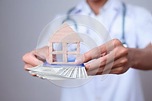 Close up of male doctor hands showing money, banknotes and shapes of miniature house isolated gray background