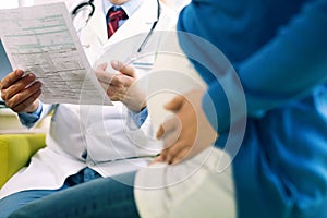 Close up of male doctor holding document with pregnant woman