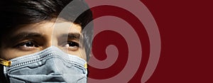 Close-up of male face wearing medical flu mask against coronavirus on dark red background with copy space.