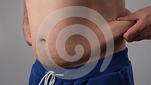 Close-up of a male fat shaking belly against a white background. The obese man touches his stomach and shows his thumb