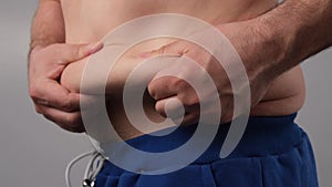 Close-up of a male fat shaking belly against a white background. The obese man touches his stomach and shows his thumb