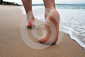 Close up of male feet and golden sand and ocean water. Summer activity and vacation holiday concept