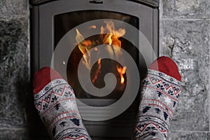 Close up of male feet legs in colored woolen socks are warming near flame, firewood burns in stove, fireplace, cozy winter evening