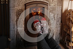 close up of male feet legs in colored woolen socks are warming near flame, firewood burns in stove, fireplace, cozy winter evening