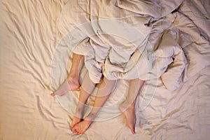 Close up of male and female feet on a bed  having sex under sheets in the bedroom