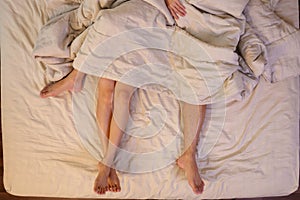 Close up of male and female feet on a bed  having sex under sheets in the bedroom