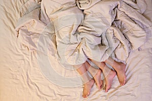 Close up of male and female feet on a bed  having sex under sheets in the bedroom