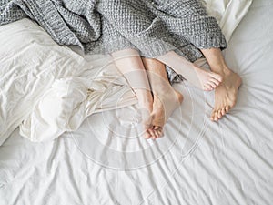 Close up of male and female feet on a bed - Loving couple under grey blanket in the bedroom - Concept of sensual and