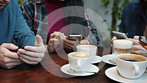 Close-up of male and female hands using smartphones touching screens at table in cafe