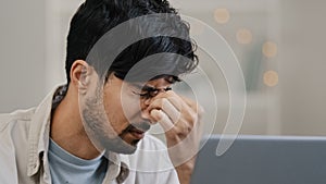 Close-up male focused arabic young guy business man freelancer looking at laptop tired discomfort in eyes pain worrying
