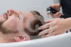 Close-up of a male hair care master washing a mans head in a sink after cutting his hair