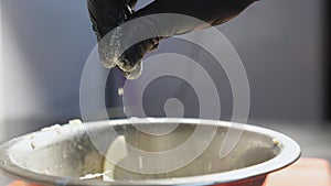 Close up male hand of chef in glove adding white salt to salad in iron bowl at kitchen. Arm of cook sprinkling spices a