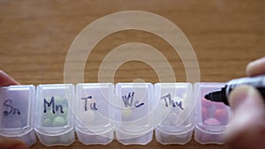 close up of male hand fingers marks cells with black marker for days of week in plastic pill organizer box. sick man
