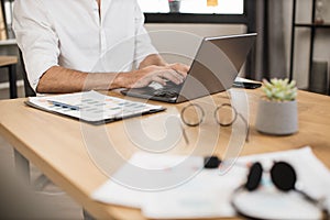 Close up of male hand in formal wear typing on modern laptop while sitting at desk.
