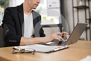 Close up of male hand in formal wear typing on modern laptop while sitting at desk.