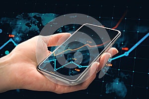 Close up of male hand holding cellphone with glowing business chart and map on dark background. Stock, global growth and financial