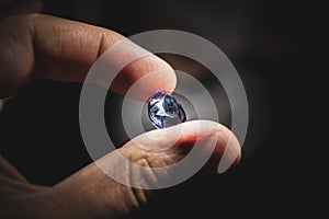 Close-up of male hand holding faceted jewelry with dark background.