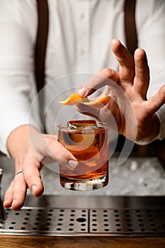 close-up of male hand holding glass with alcoholic drink and garnishing it with orange zest