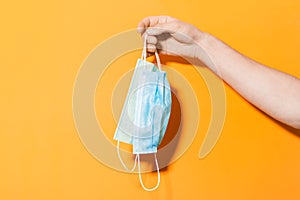 Close-up of male hand, holding medical flu masks, isolated on orange background.