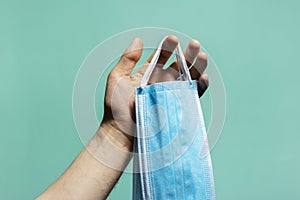 Close-up of male hand holding medical flu masks preventing coronavirus on background of cyan, aqua menthe color with shadows.