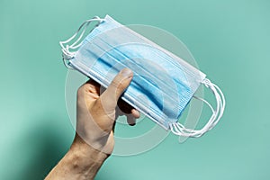 Close-up of male hand holding medical flu masks preventing coronavirus on background of cyan, aqua menthe color with shadows.