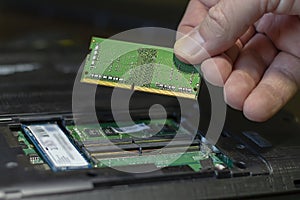 Close-up of a male hand holding a RAM card on the background of a disassembled laptop.