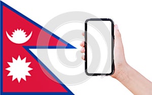 Close-up of male hand holding smartphone with blank on screen, on background of blurred flag of Nepal