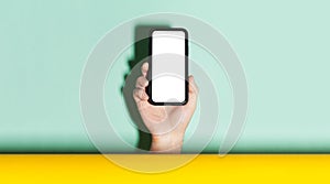 Close-up of male hand holding smartphone with mockup between two backgrounds of yellow and aqua menthe color.