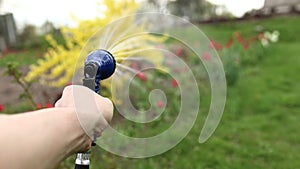 close up male hand holding water hose and watering lawn or plants on backyard. gardener man with sprinkler in garden