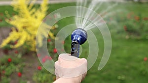 close up male hand holding water hose and watering lawn or plants on backyard. gardener man with sprinkler in garden