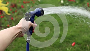 close up male hand holding water hose and watering lawn or plants on backyard. gardener man with sprinkler in garden