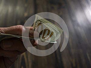 Close up of male hand holds two banknotes of hundred dollars on a wooden background. new hundred-dollar bills.Money USA dollar